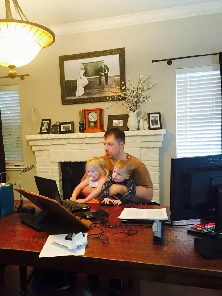 Work and family, never far from each other. Mark C. Smith working at his home desk with one of his young children seated on his lap.