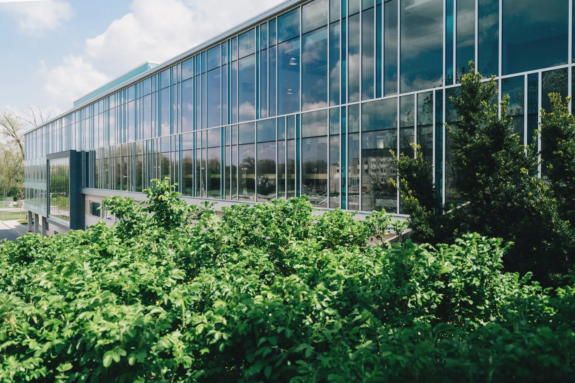 A large building with many windows and shrubbery in front.
